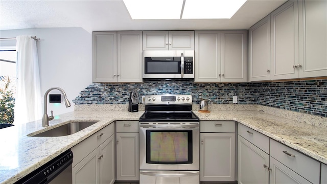 kitchen featuring light stone countertops, stainless steel appliances, sink, gray cabinets, and backsplash