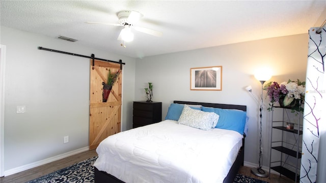 bedroom featuring hardwood / wood-style flooring, ceiling fan, a barn door, and a textured ceiling