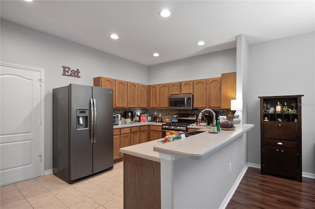 kitchen with sink, stainless steel appliances, kitchen peninsula, decorative backsplash, and light tile patterned floors