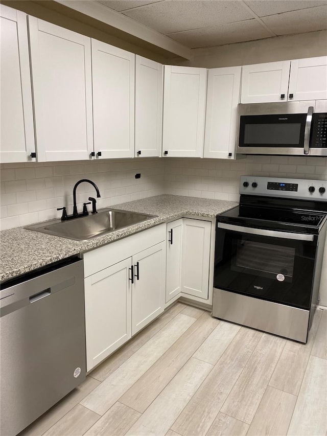 kitchen with appliances with stainless steel finishes, light hardwood / wood-style flooring, sink, and white cabinets