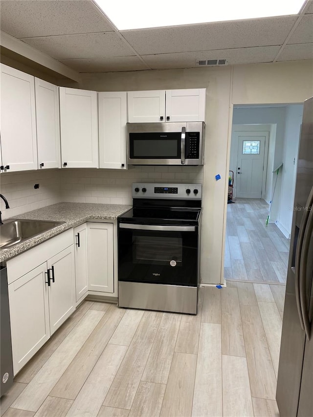 kitchen with decorative backsplash, stainless steel appliances, white cabinets, a paneled ceiling, and light hardwood / wood-style floors