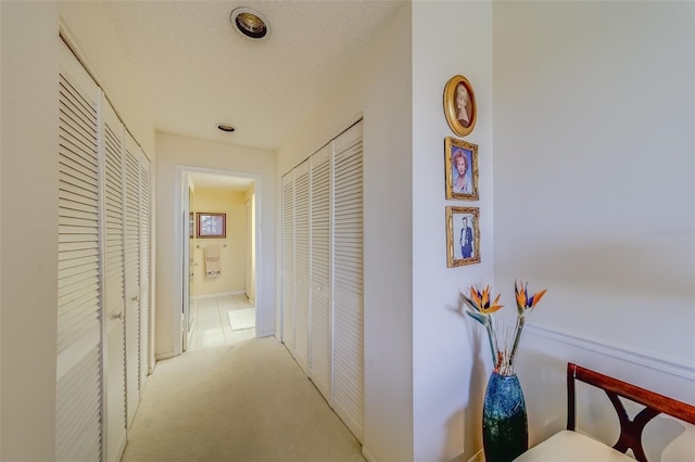 hall with light colored carpet and a textured ceiling