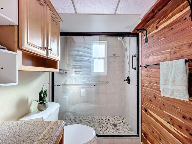 bathroom with vanity, toilet, a shower with door, and wood walls