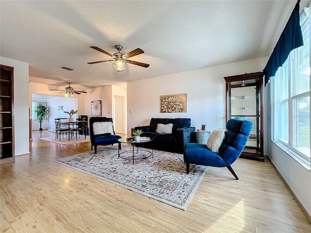 living room with a textured ceiling, light hardwood / wood-style floors, and ceiling fan