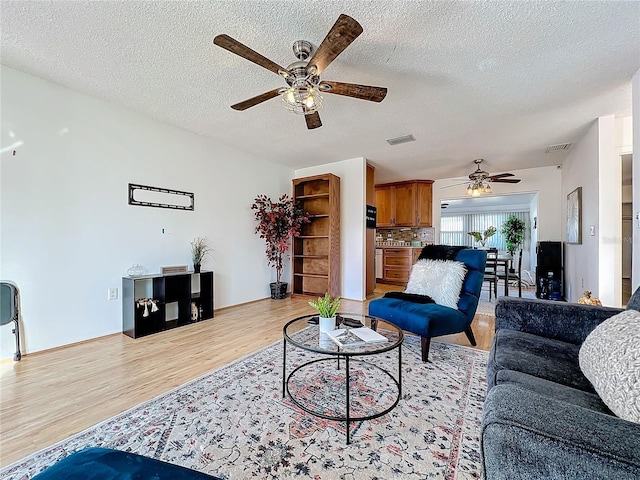 living room featuring light wood-type flooring, a textured ceiling, and ceiling fan