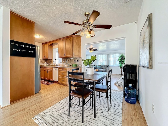 dining room featuring ceiling fan, sink, light hardwood / wood-style floors, and a textured ceiling