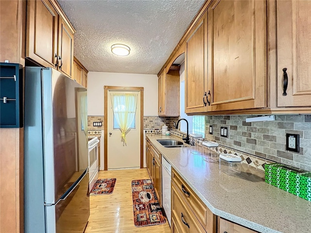 kitchen featuring sink, stainless steel fridge, stove, light hardwood / wood-style floors, and dishwashing machine