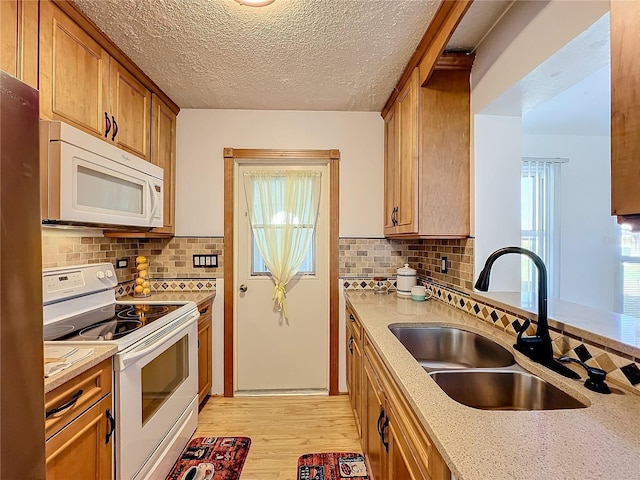 kitchen with white appliances, backsplash, sink, light hardwood / wood-style flooring, and a textured ceiling