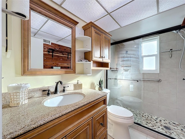 bathroom featuring a paneled ceiling, vanity, a shower with door, tile patterned flooring, and toilet