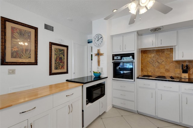 kitchen featuring decorative backsplash, light tile patterned floors, white cabinetry, a textured ceiling, and black appliances