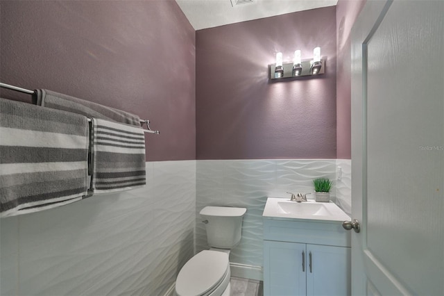 bathroom with vanity, toilet, and tile walls