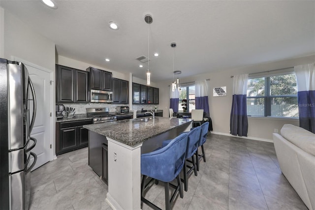 kitchen with appliances with stainless steel finishes, sink, backsplash, decorative light fixtures, and a kitchen island with sink