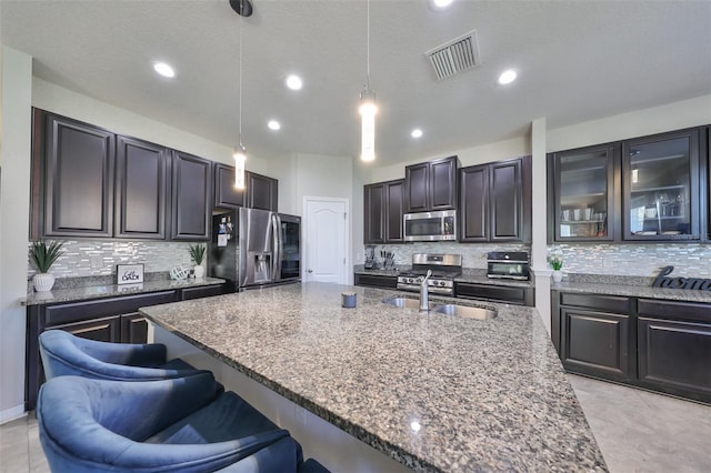 kitchen featuring tasteful backsplash, appliances with stainless steel finishes, decorative light fixtures, and a breakfast bar area