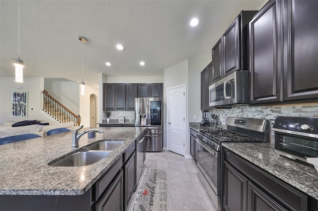 kitchen with tasteful backsplash, hanging light fixtures, a center island with sink, sink, and stainless steel appliances