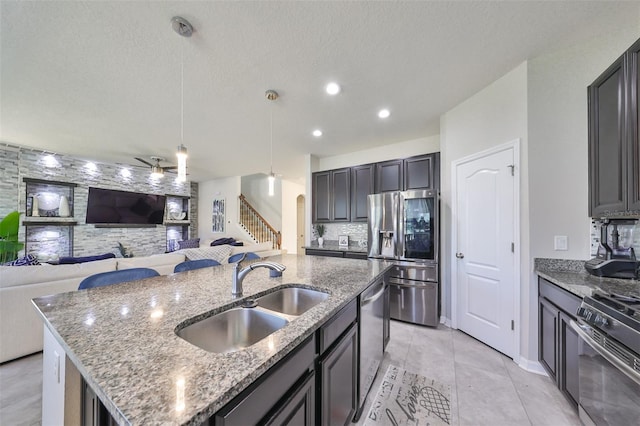 kitchen featuring stone countertops, hanging light fixtures, a center island with sink, sink, and appliances with stainless steel finishes