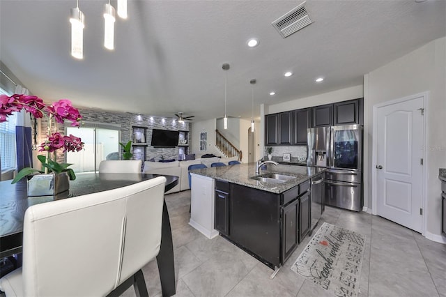 kitchen featuring a kitchen island with sink, sink, pendant lighting, appliances with stainless steel finishes, and light stone counters