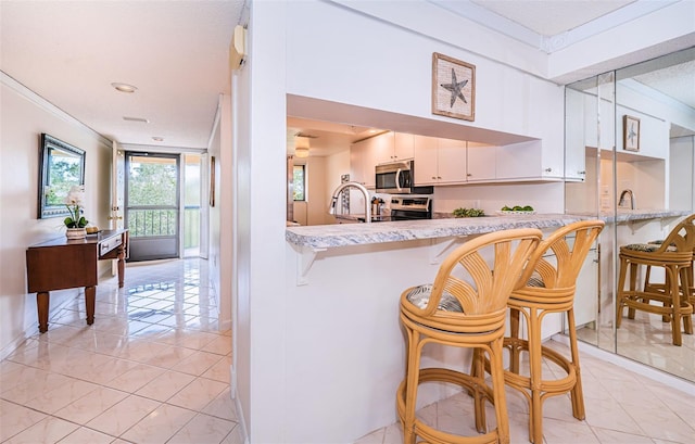 kitchen featuring stainless steel appliances, kitchen peninsula, ornamental molding, a kitchen breakfast bar, and white cabinets