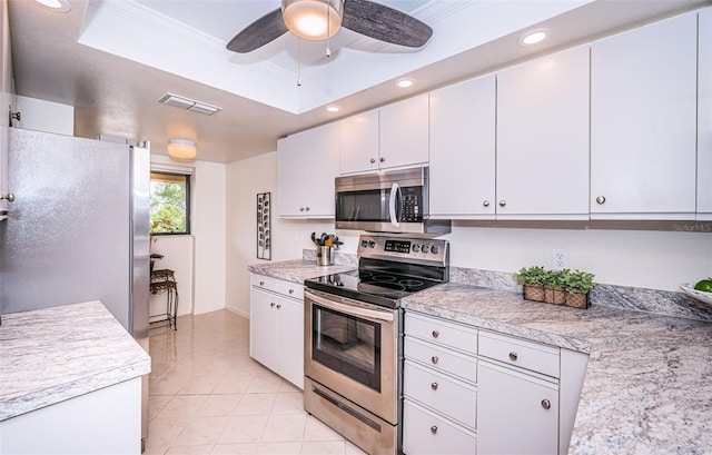 kitchen featuring stainless steel appliances, white cabinetry, ceiling fan, a tray ceiling, and crown molding