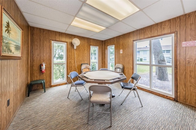 dining area featuring a drop ceiling, carpet, and wood walls