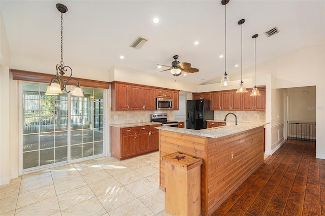 kitchen featuring a center island with sink, appliances with stainless steel finishes, light stone countertops, and decorative light fixtures