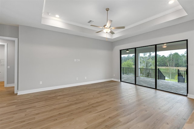 empty room with a raised ceiling, crown molding, light hardwood / wood-style flooring, and ceiling fan