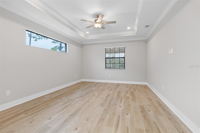 empty room with ornamental molding, ceiling fan, a tray ceiling, and light hardwood / wood-style flooring