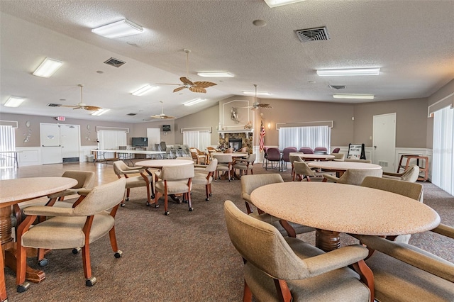 carpeted dining area with lofted ceiling, a textured ceiling, a fireplace, and ceiling fan