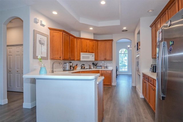 kitchen with sink, white appliances, hardwood / wood-style flooring, backsplash, and a raised ceiling