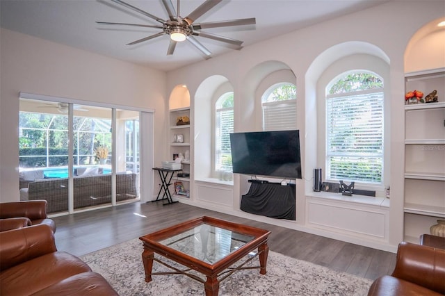 living room with wood-type flooring, ceiling fan, and built in shelves