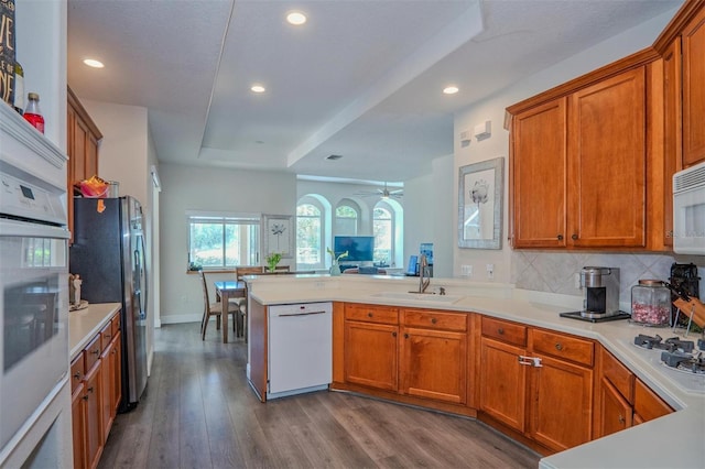 kitchen with sink, white appliances, decorative backsplash, kitchen peninsula, and light wood-type flooring