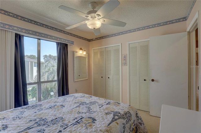 carpeted bedroom with a textured ceiling, multiple closets, and ceiling fan