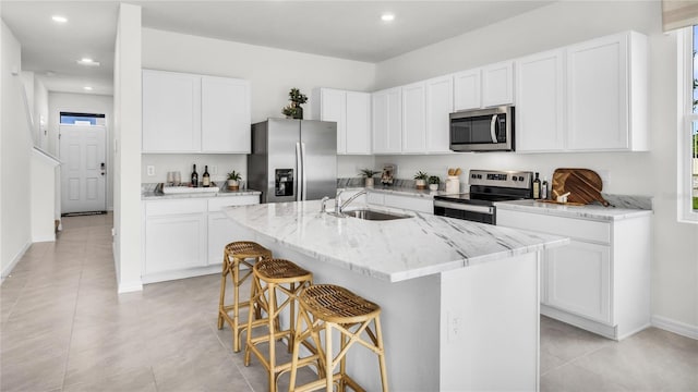 kitchen featuring a breakfast bar area, light stone counters, an island with sink, white cabinets, and appliances with stainless steel finishes