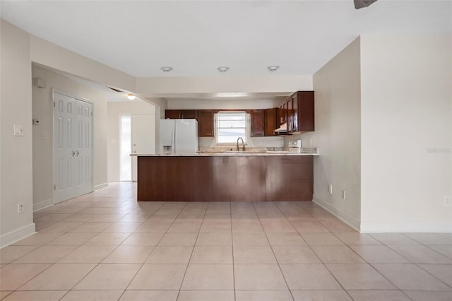 kitchen with kitchen peninsula, light tile patterned flooring, white refrigerator with ice dispenser, and sink