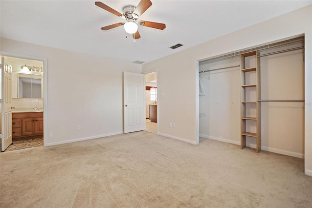 unfurnished bedroom featuring ceiling fan, light colored carpet, a closet, and ensuite bath