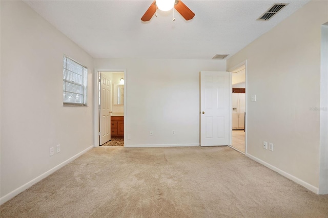 unfurnished bedroom with ensuite bath, light carpet, white refrigerator with ice dispenser, and ceiling fan