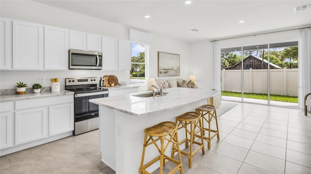 kitchen with white cabinets, an island with sink, sink, appliances with stainless steel finishes, and a breakfast bar area