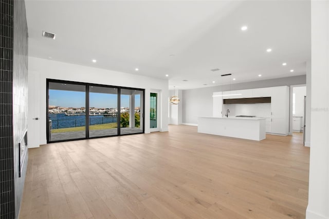 unfurnished living room with sink, a water view, and light hardwood / wood-style floors