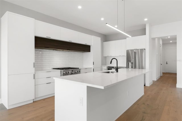 kitchen featuring tasteful backsplash, appliances with stainless steel finishes, sink, light hardwood / wood-style flooring, and a center island with sink