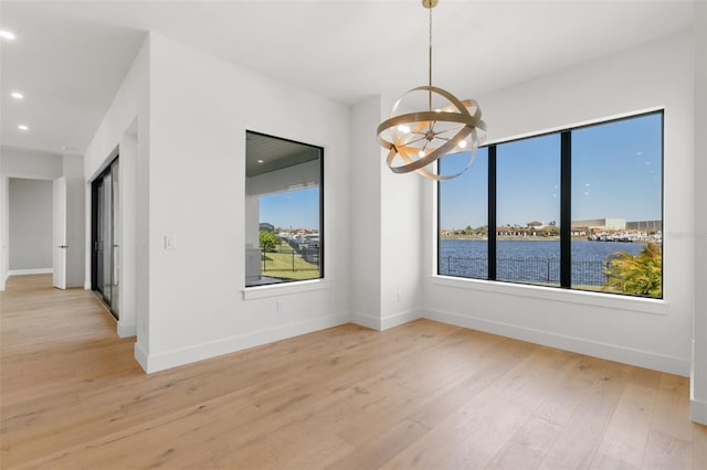 unfurnished dining area featuring a wealth of natural light, a chandelier, light hardwood / wood-style flooring, and a water view