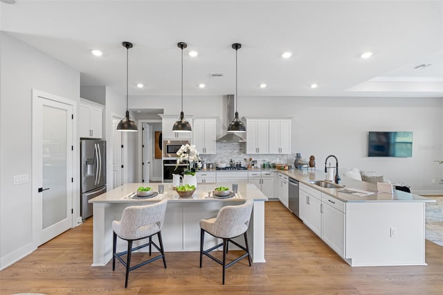 kitchen with wall chimney exhaust hood, light hardwood / wood-style floors, pendant lighting, white cabinetry, and appliances with stainless steel finishes