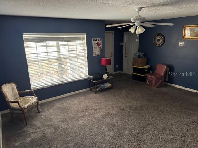 sitting room with a textured ceiling, ceiling fan, and dark carpet