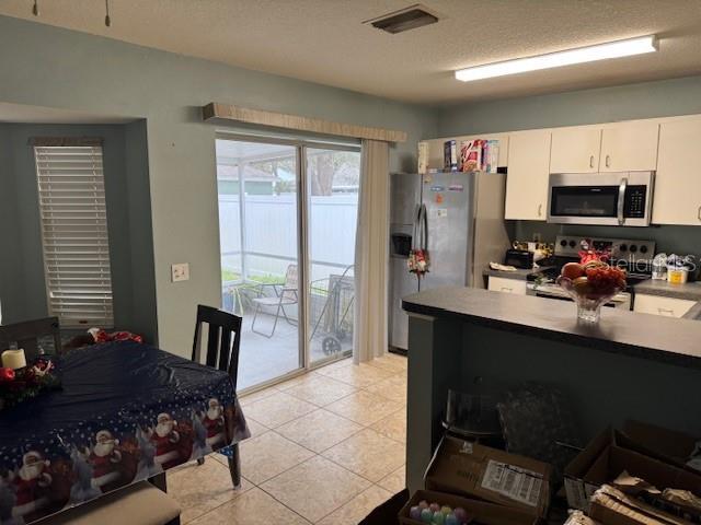 kitchen with stainless steel appliances, white cabinets, a textured ceiling, and light tile patterned floors