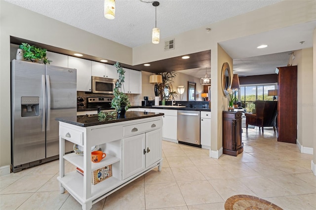 kitchen with white cabinetry, stainless steel appliances, hanging light fixtures, light tile patterned floors, and a textured ceiling