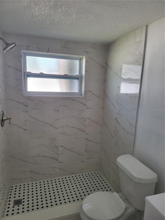 bathroom with a tile shower, vanity, a textured ceiling, and toilet