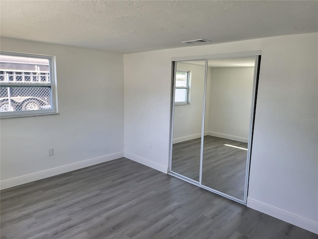 unfurnished bedroom with a textured ceiling, a closet, dark hardwood / wood-style flooring, and multiple windows