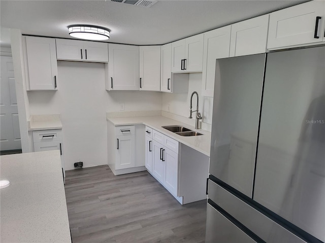 kitchen with white cabinets, sink, a textured ceiling, stainless steel refrigerator, and light hardwood / wood-style floors