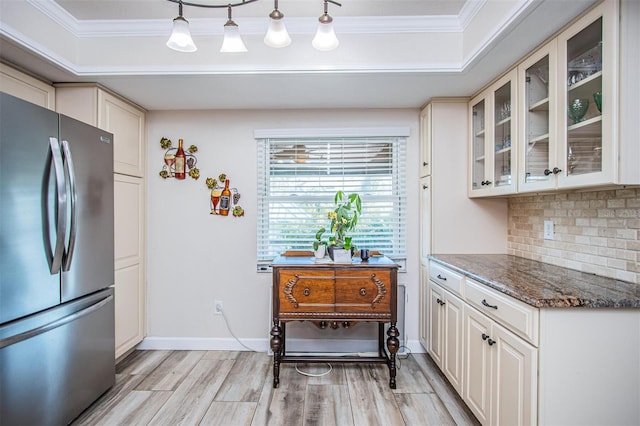 kitchen featuring dark stone countertops, ornamental molding, stainless steel fridge, light wood-type flooring, and tasteful backsplash