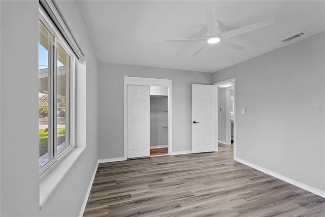 unfurnished bedroom with light hardwood / wood-style flooring, a closet, a walk in closet, and ceiling fan