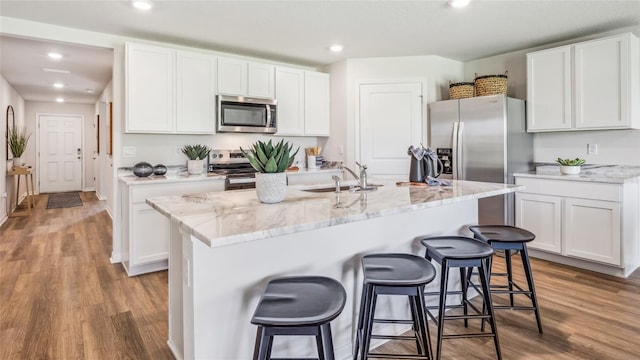 kitchen featuring stainless steel appliances, sink, dark hardwood / wood-style flooring, white cabinetry, and a center island with sink