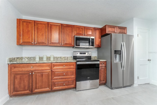 kitchen with a textured ceiling, light stone counters, stainless steel appliances, and light tile patterned floors